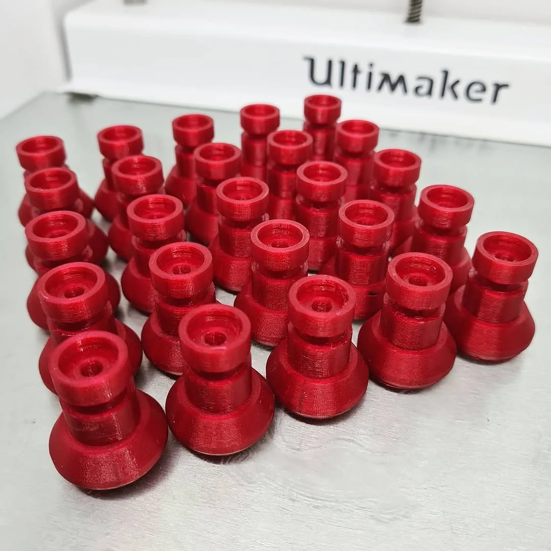 Mini serija istovetnih crvenih 3D štampanih rezervnih delova od PETG-a, ispred štampača Ultimaker