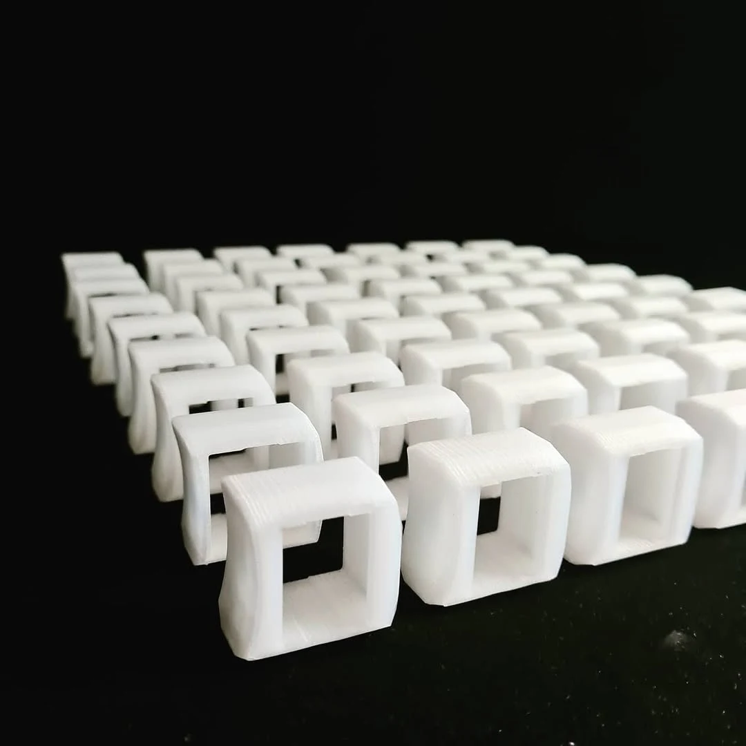 A small series of identical white 3D-printed spare parts arranged in rows on a black surface