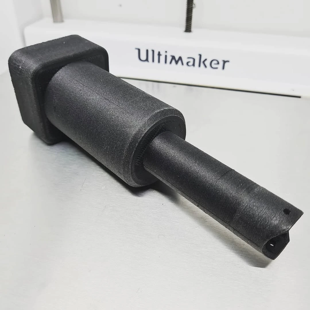Schwarzer 3D-gedruckter Prototyp aus Carbon-Verbundwerkstoff vor einem Ultimaker-Drucker