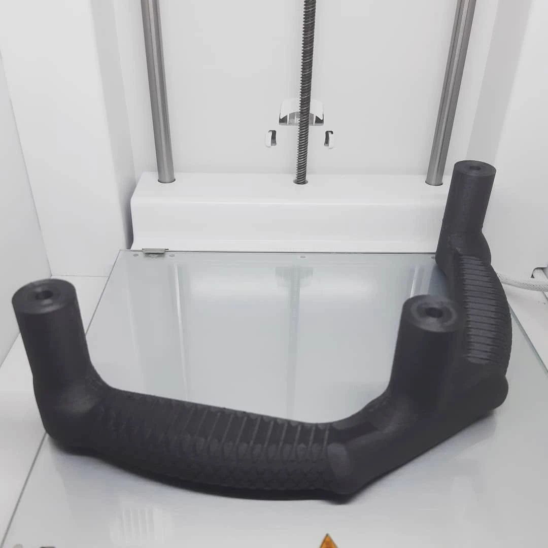 Dunkelgrauer 3D-gedruckter Prototyp eines Griffs mit geripptem Griffstück, auf dem Druckbett