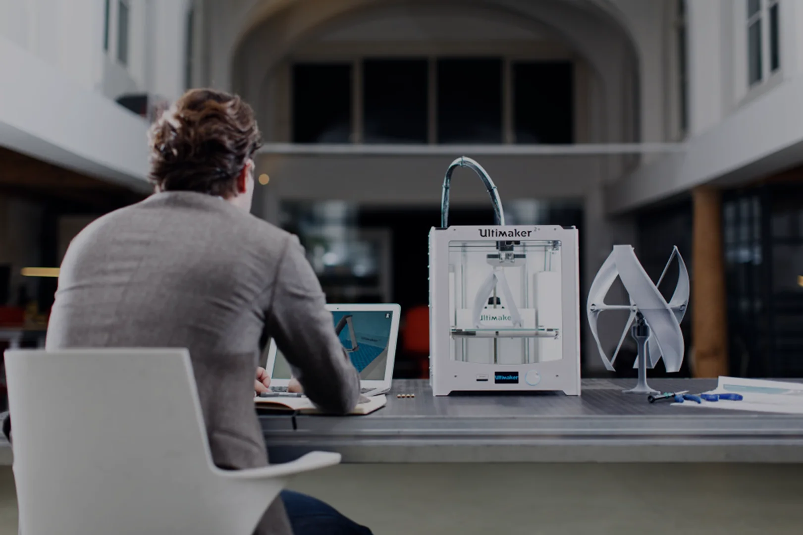 Working on a 3D model at a computer, next to a 3D printer and a printed part