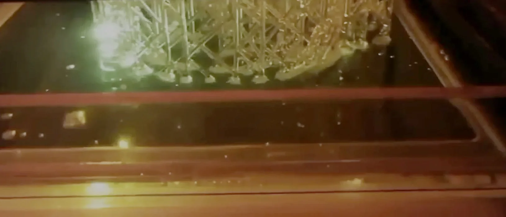 SLA 3D printing in progress — a laser cures a layer of resin beneath a part with a support structure